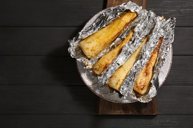 Photo of Tasty baked parsnips on black wooden table, top view. Space for text