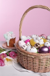 Wicker basket with festively decorated Easter eggs and beautiful tulips on white marble table against pink background