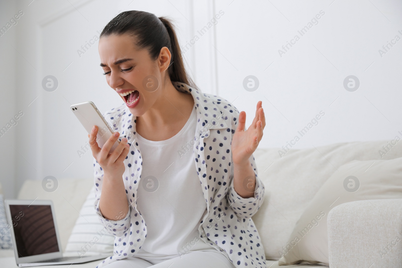 Photo of Emotional young woman talking on smartphone at home. Hate concept