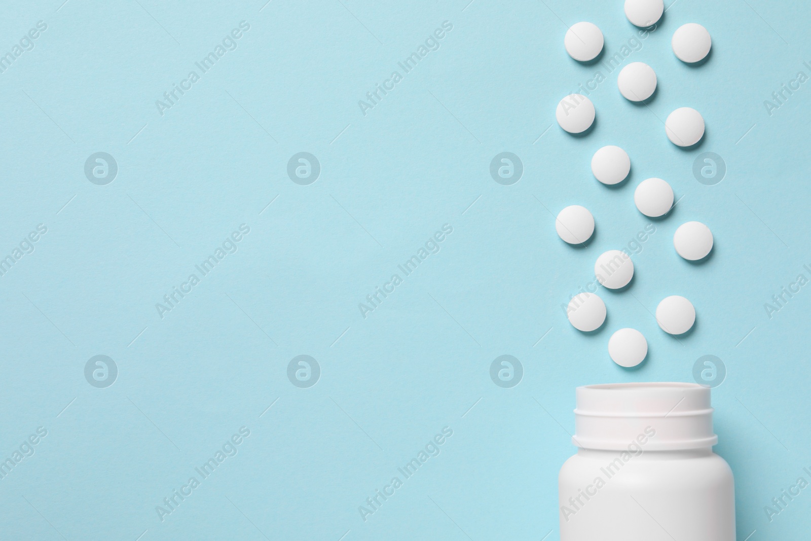 Photo of Plastic bottle with many white pills on light blue background, flat lay. Space for text