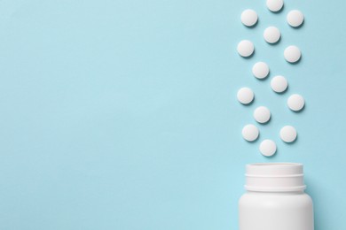 Photo of Plastic bottle with many white pills on light blue background, flat lay. Space for text