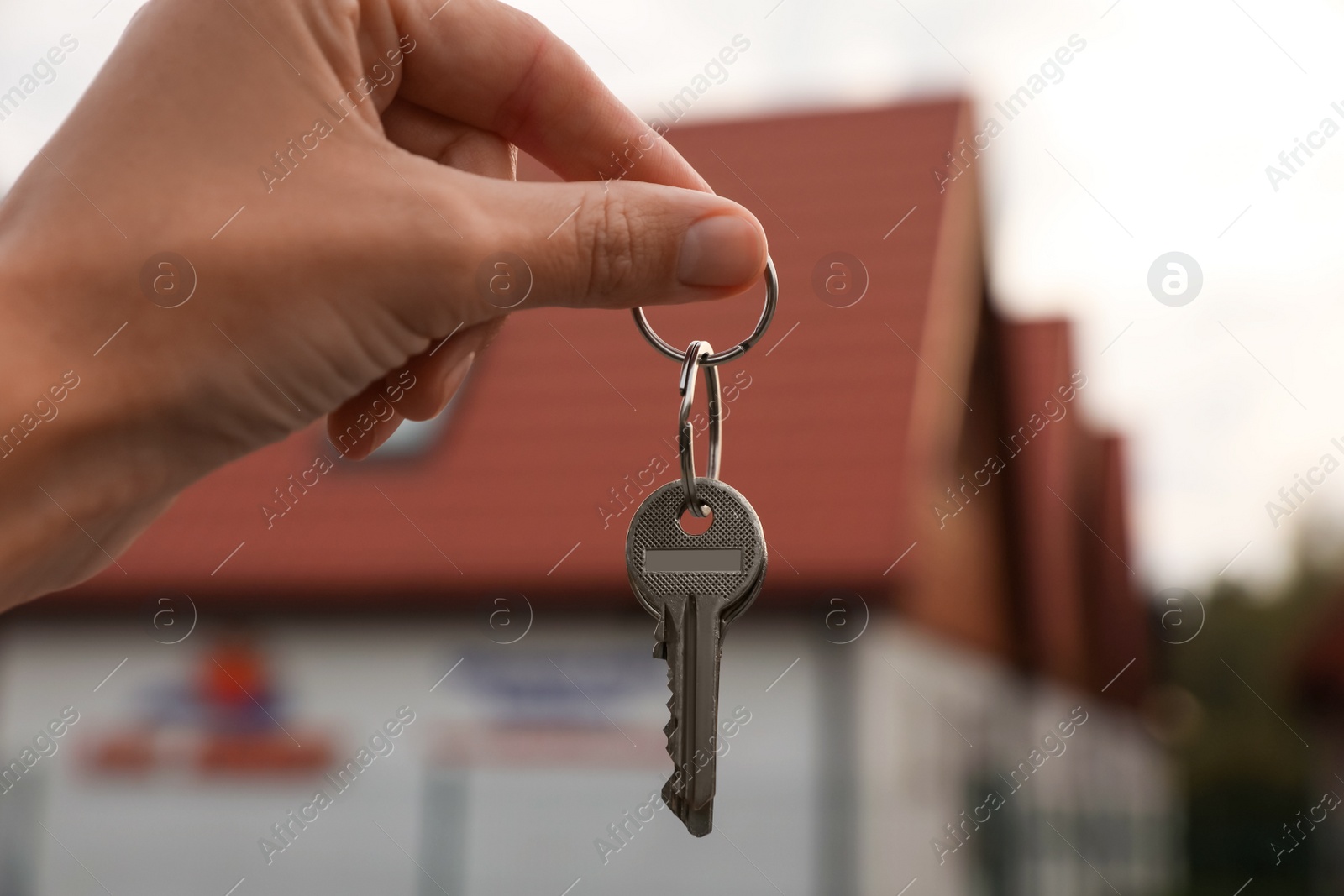 Photo of Real estate agent holding keys to new house outdoors, closeup