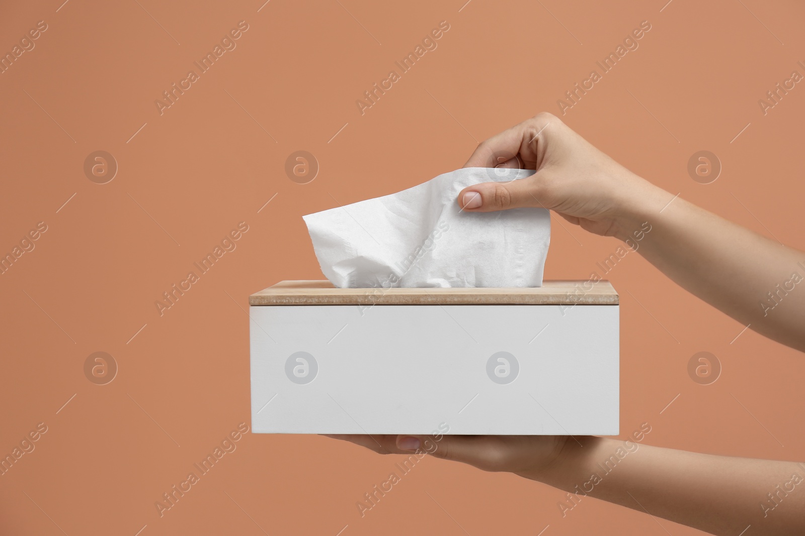 Photo of Woman taking paper tissue from holder on light brown background, closeup