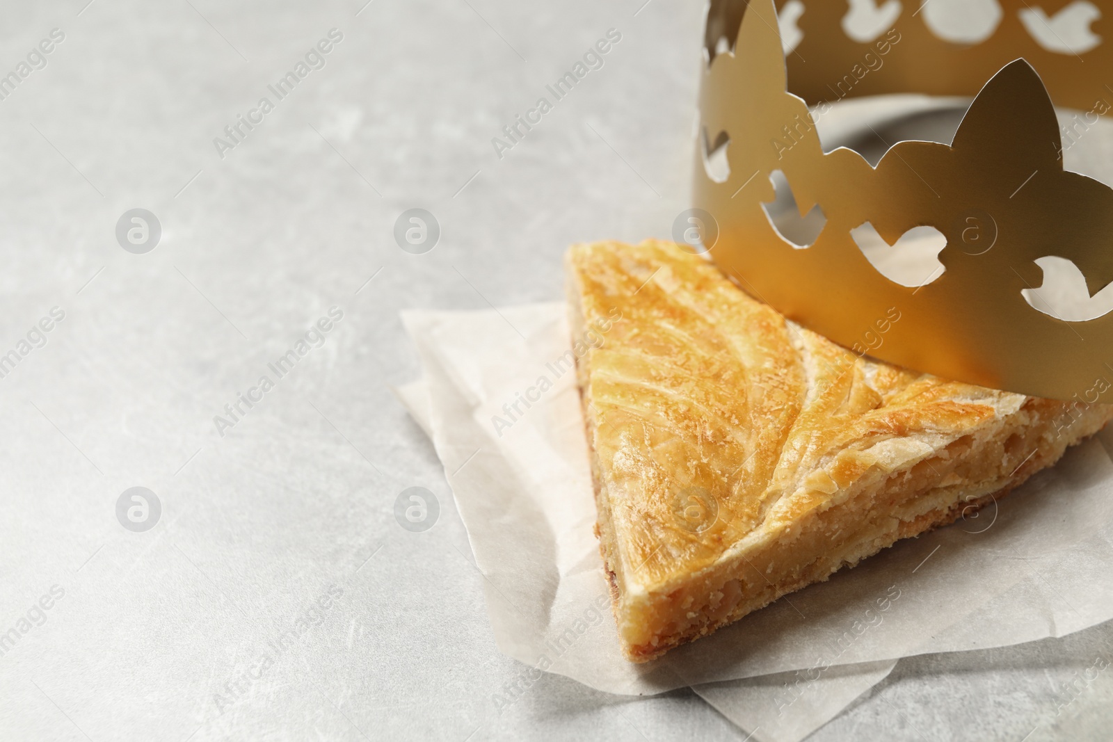 Photo of Slice of traditional galette des Rois with paper crown on light grey table. Space for text