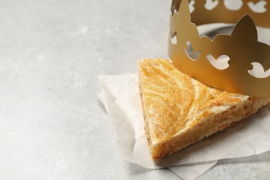 Photo of Slice of traditional galette des Rois with paper crown on light grey table. Space for text