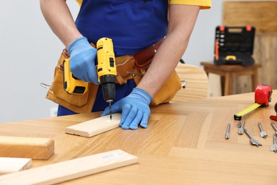 Young worker using electric drill at table in workshop, closeup