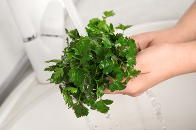 Photo of Woman washing bunch of fresh parsley under tap water in kitchen sink, closeup
