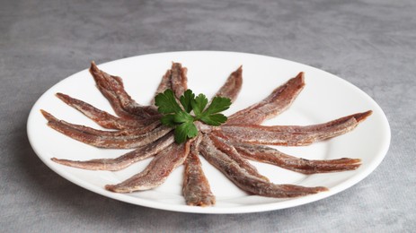 Plate with anchovy fillets and parsley on grey table, closeup