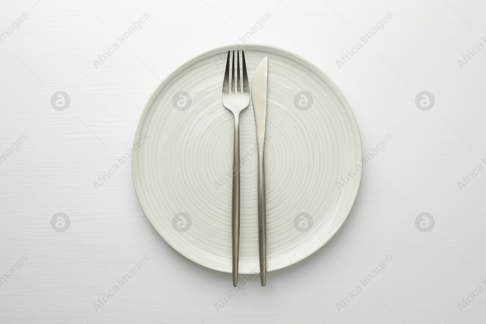 Photo of Clean plate, fork and knife on white table, top view