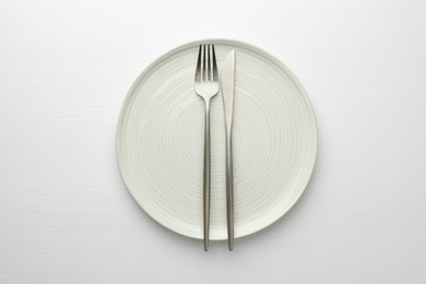 Clean plate, fork and knife on white table, top view