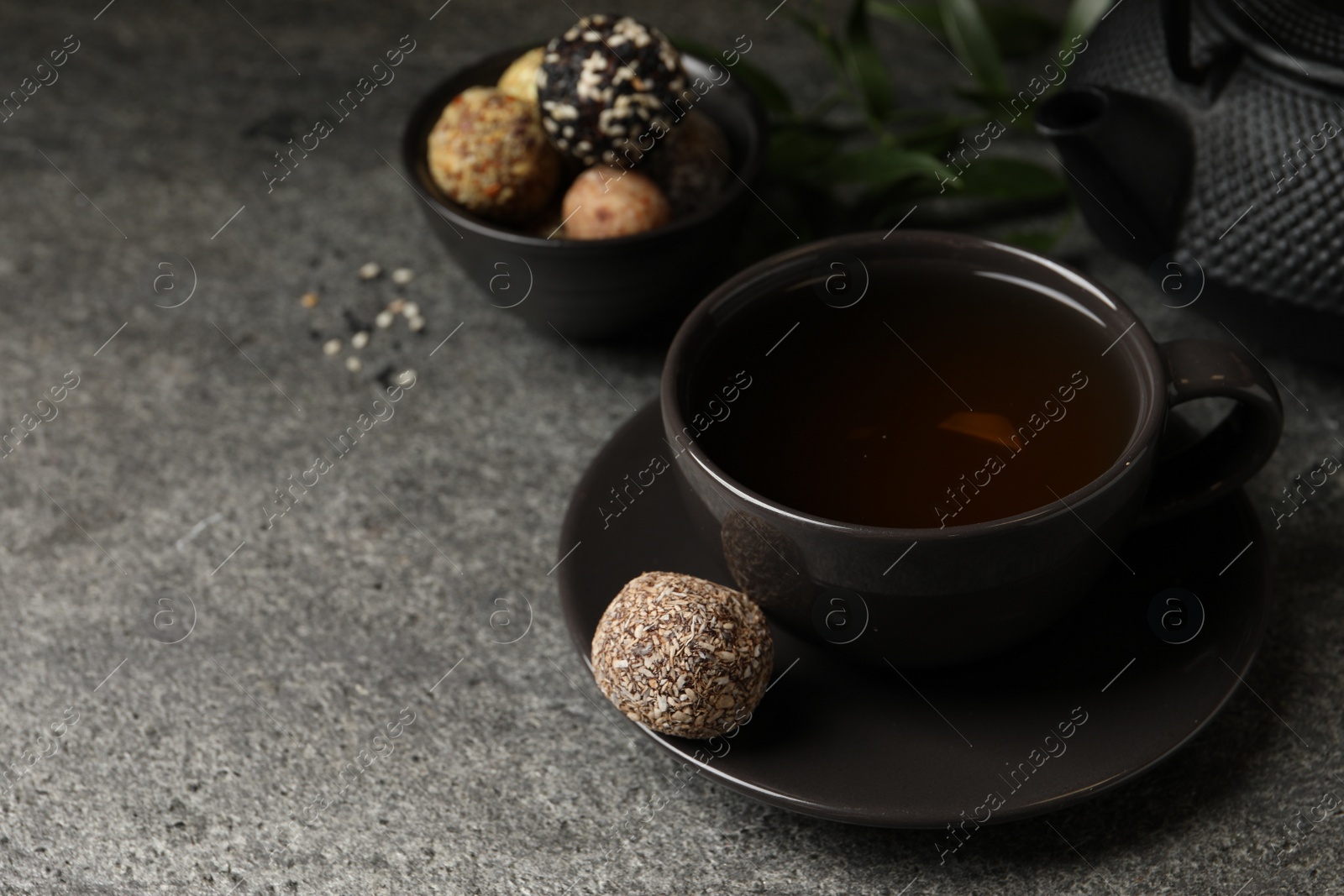 Photo of Cup of aromatic tea and delicious vegan candy balls on grey table, space for text