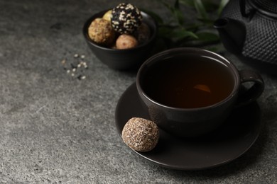 Cup of aromatic tea and delicious vegan candy balls on grey table, space for text