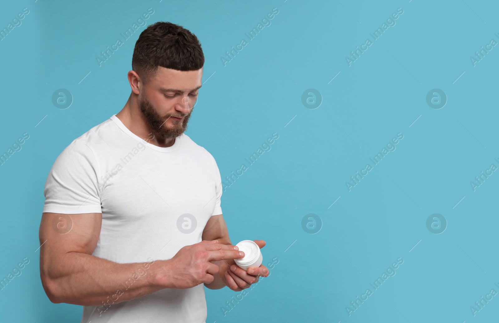 Photo of Handsome man applying body cream on light blue background, space for text