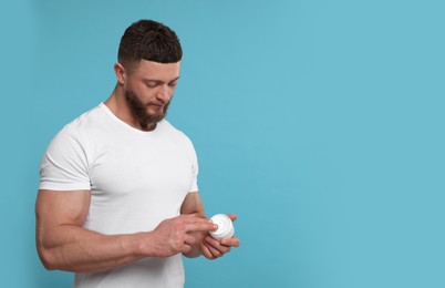 Handsome man applying body cream on light blue background, space for text