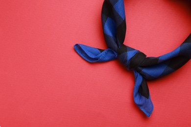 Photo of Tied blue bandana with check pattern on red background, top view. Space for text