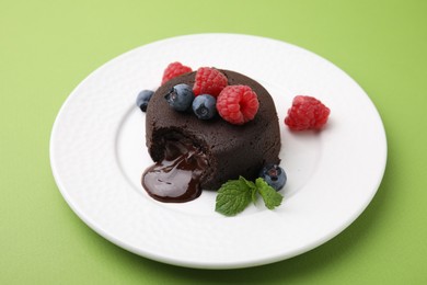 Photo of Plate with delicious chocolate fondant, berries and mint on light green table