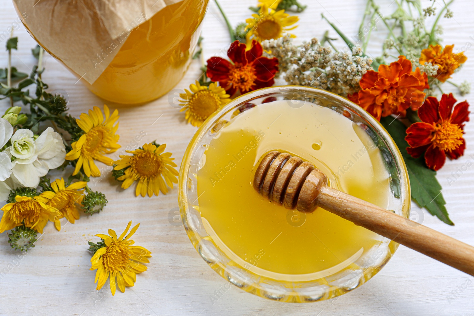 Photo of Honey with dipper in bowl and different flowers on white wooden table, closeup