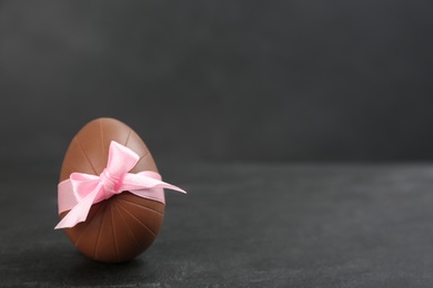 Photo of Sweet chocolate egg with pink bow on black table. Space for text