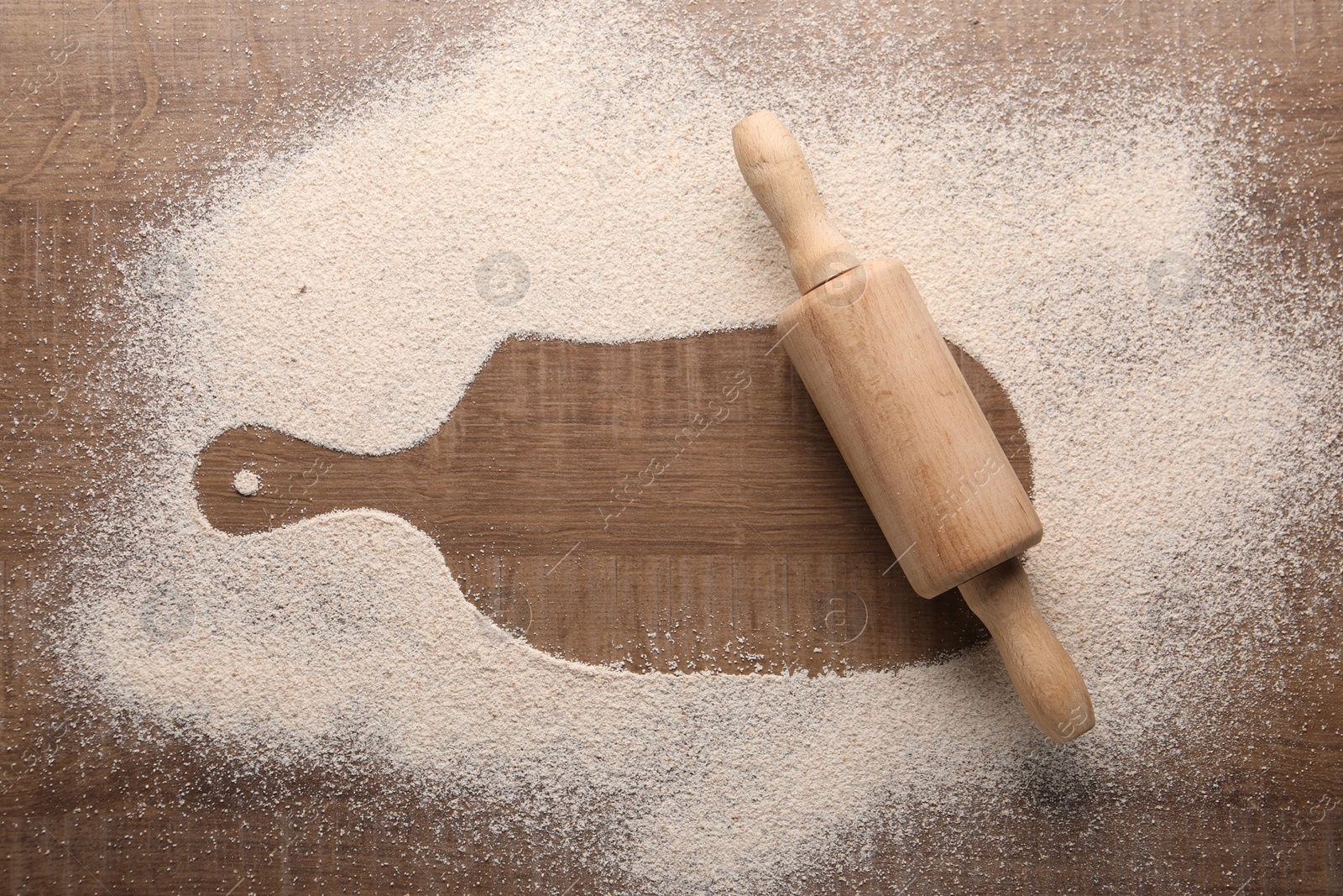 Photo of Imprint of board on wooden table with flour and rolling pin, top view