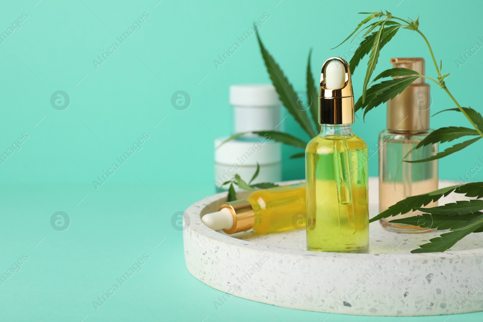 Photo of Bottles of hemp cosmetics and green leaves on turquoise background, space for text