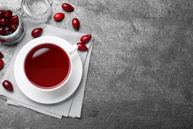 Photo of Cup of fresh dogwood tea and berries on grey table, flat lay. Space for text