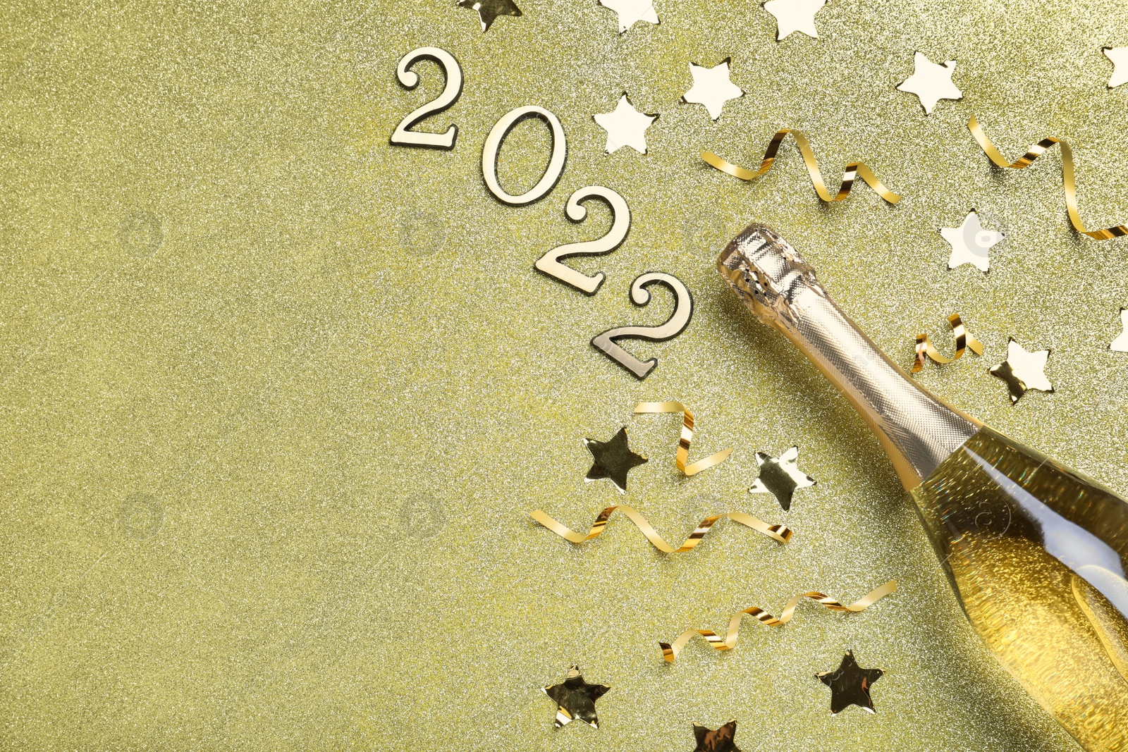 Photo of Bottle of sparkling wine, festive decor and number 2022 on golden background, flat lay with space for text. Happy New Year
