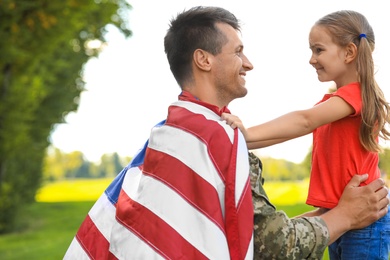 Photo of Father in military uniform with American flag and his daughter at sunny park