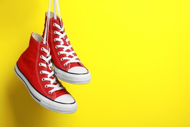 Photo of Pair of new stylish red sneakers hanging on laces against yellow background. Space for text