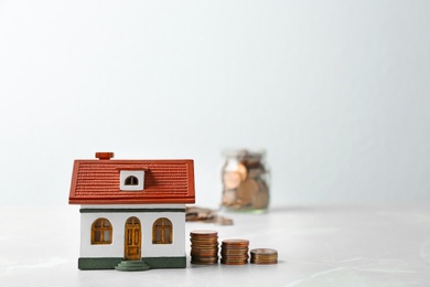 House model and coins on table against light background. Space for text