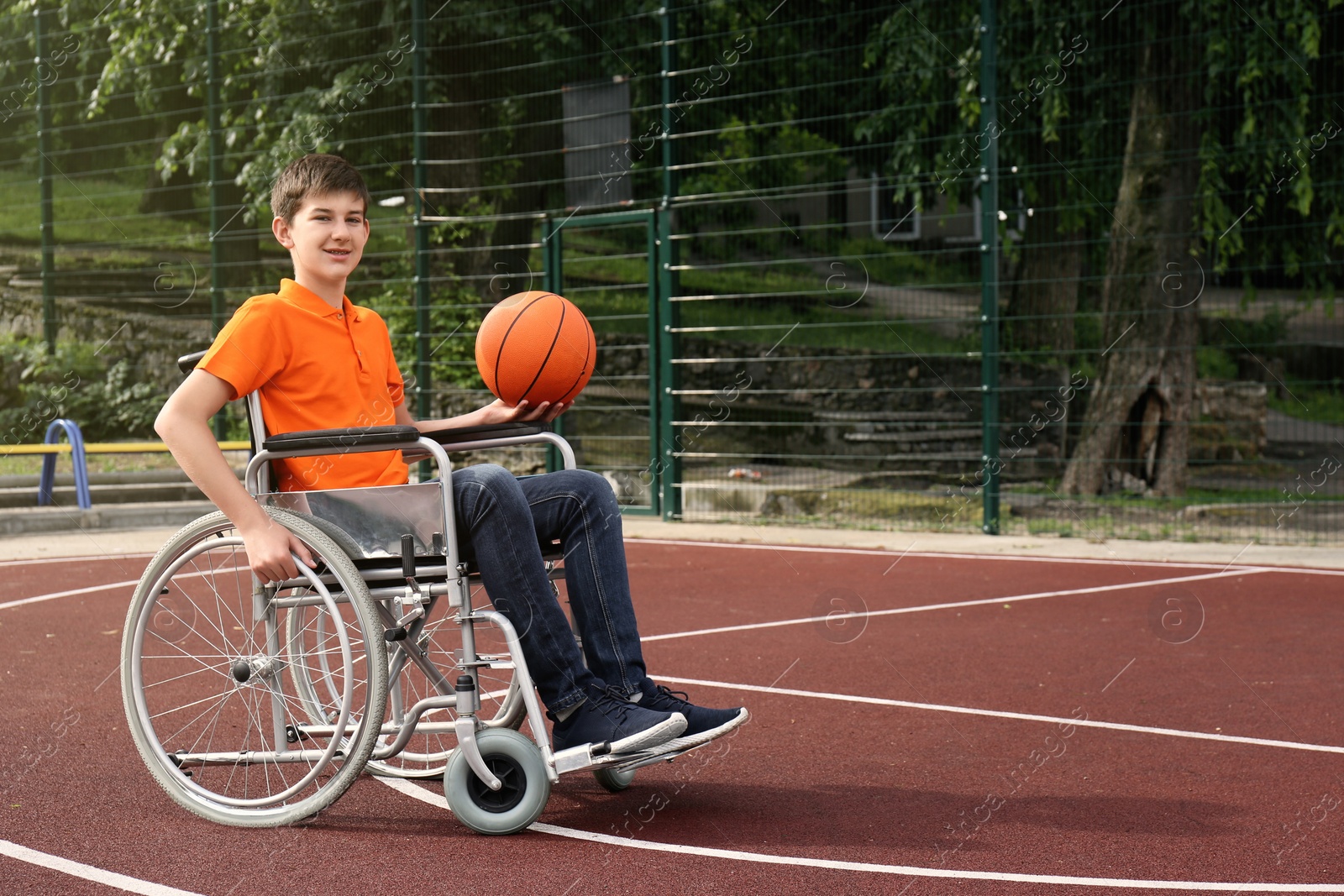 Photo of Disabled teenage boy in wheelchair with basketball ball at outdoor court