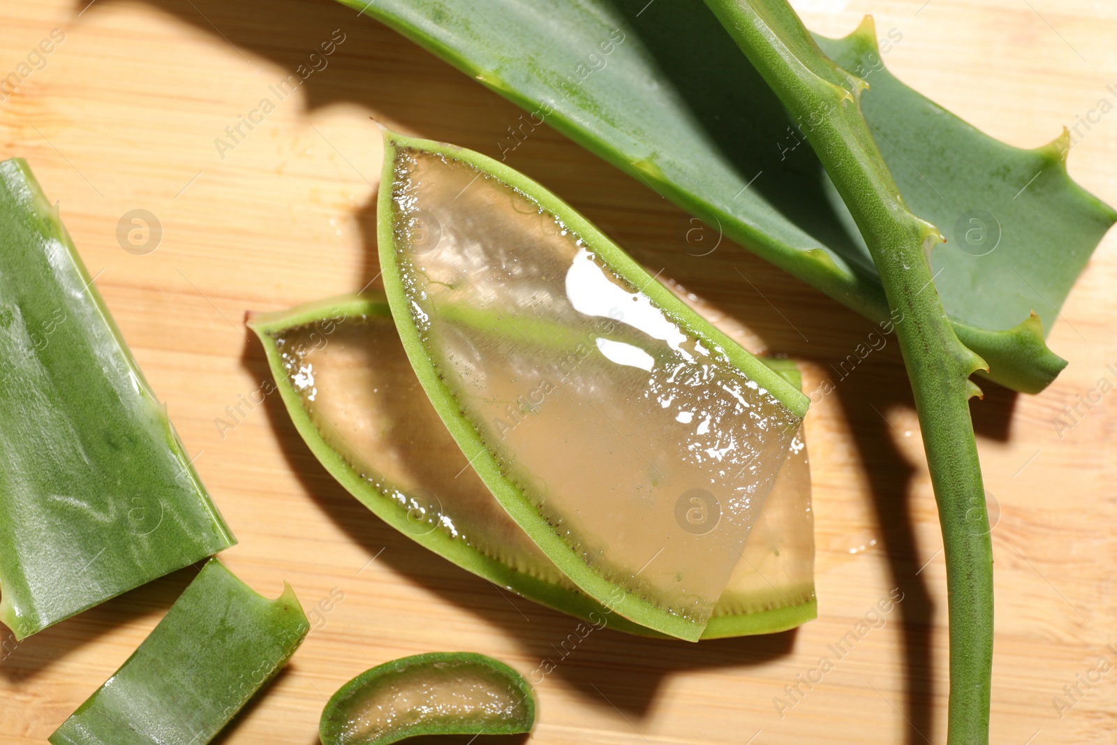 Photo of Slices of fresh aloe vera leaves with gel on wooden table, flat lay