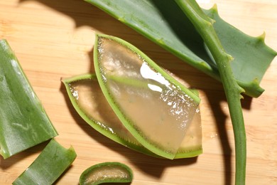 Slices of fresh aloe vera leaves with gel on wooden table, flat lay