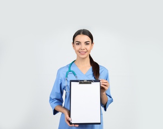 Portrait of medical assistant with stethoscope and clipboard on light background. Space for text