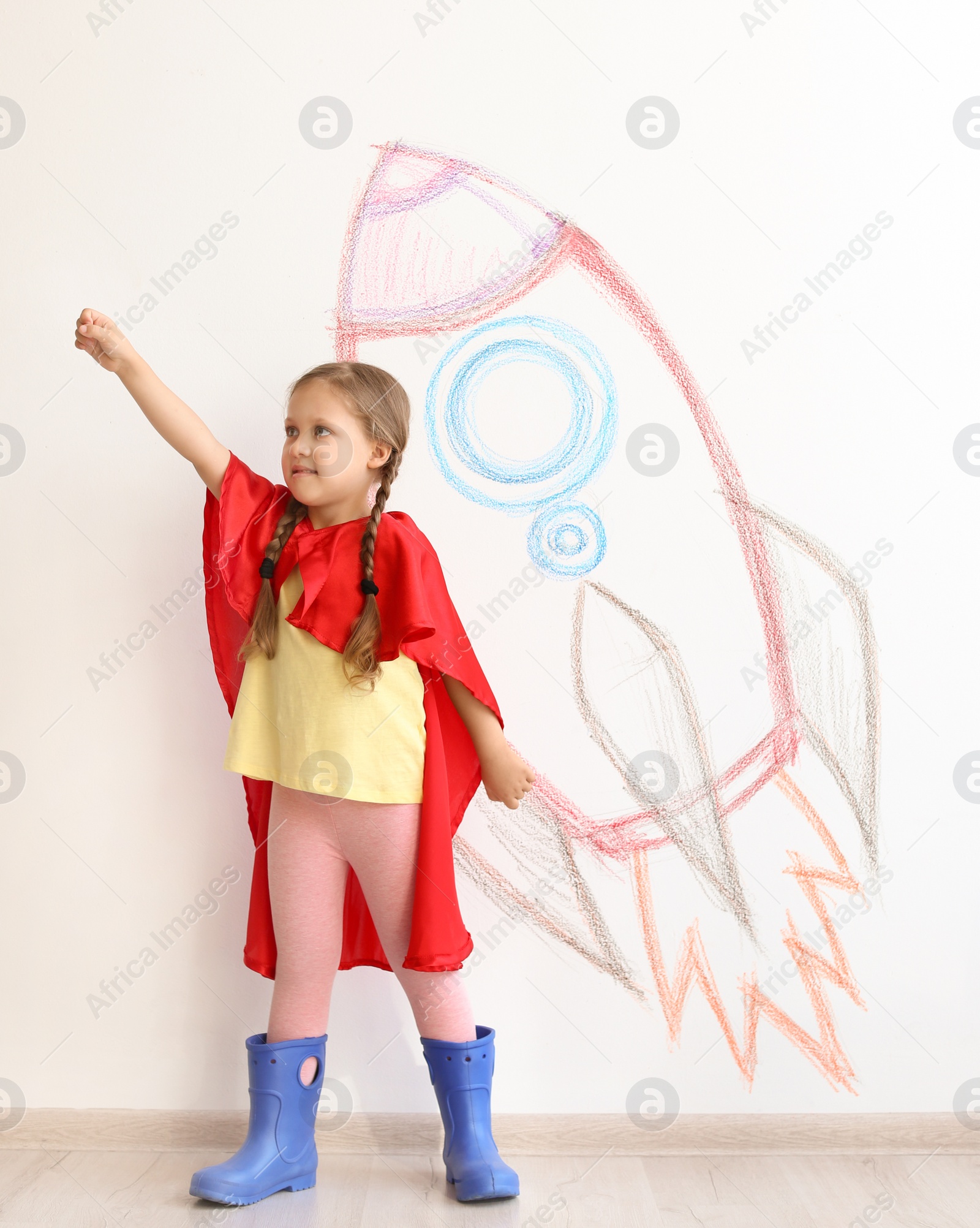 Photo of Adorable little child playing astronaut near wall with drawing of spaceship indoors