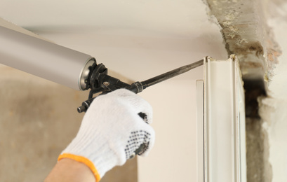 Photo of Worker using foam gun for window installation indoors, closeup