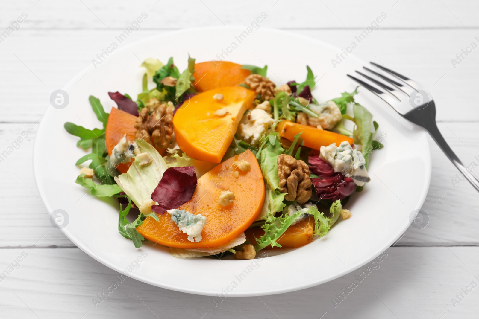 Photo of Delicious persimmon salad and fork on white wooden table, closeup