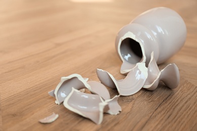 Broken pink ceramic vase on wooden floor. Space for text