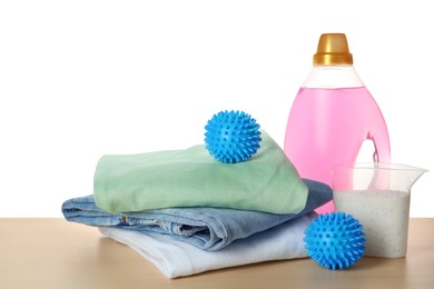 Photo of Dryer balls, detergents and stacked clean clothes on wooden table against white background