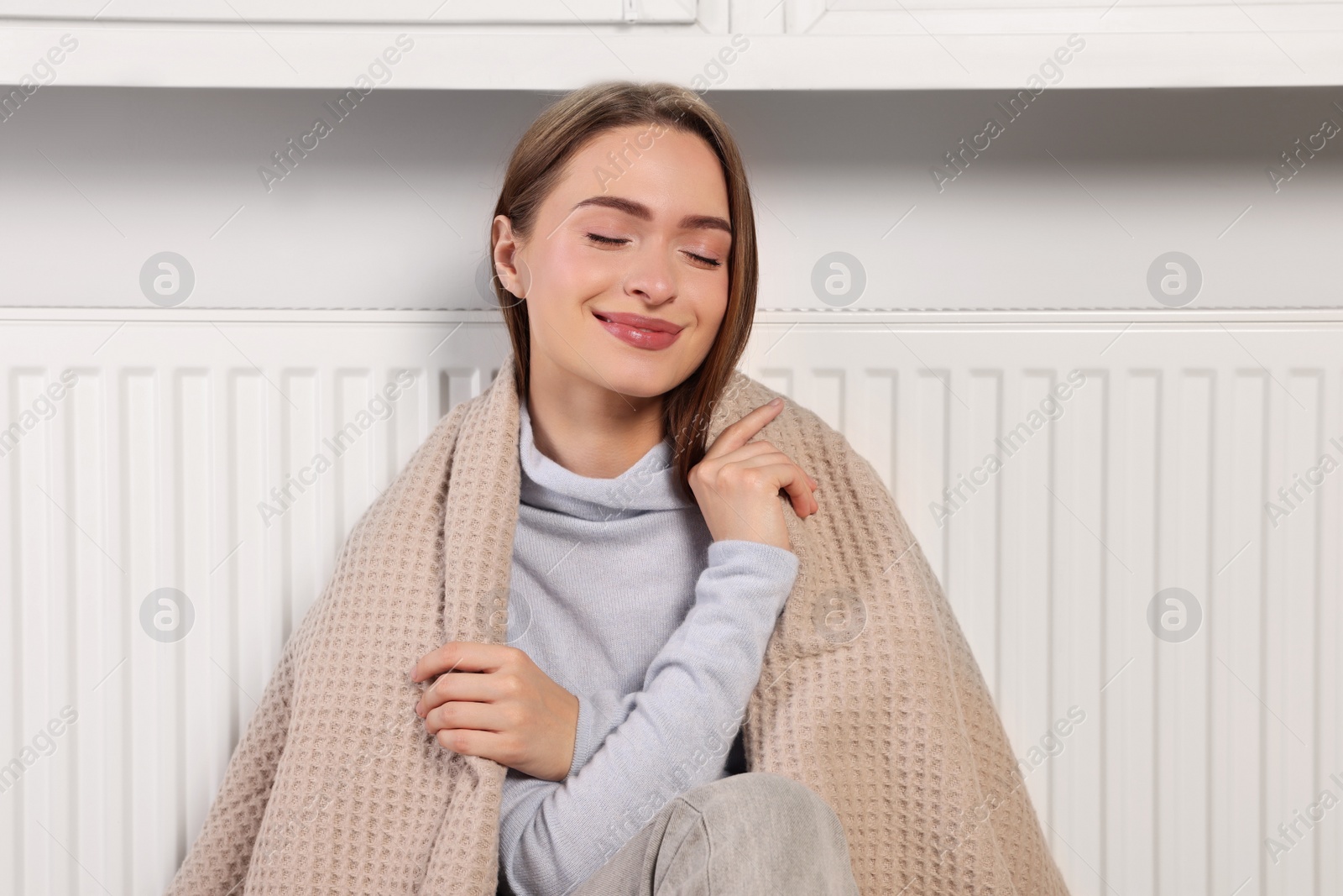 Photo of Woman with blanket sitting near heating radiator indoors