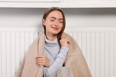 Photo of Woman with blanket sitting near heating radiator indoors