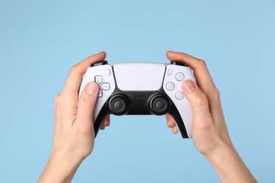 Woman using game controller on light blue background, closeup