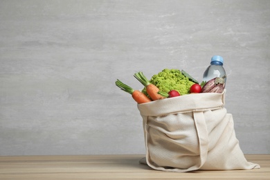 Cloth bag with vegetables and bottle of water on table against grey background. Space for text