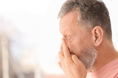 Photo of Senior man putting contact lens in his eye on blurred background