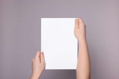 Photo of Woman holding sheet of paper on grey background, closeup. Mockup for design