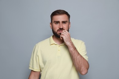 Photo of Man biting his nails on grey background. Bad habit