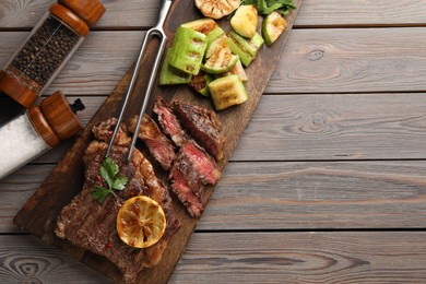 Photo of Delicious grilled beef steak and vegetables served on wooden table, flat lay. Space for text