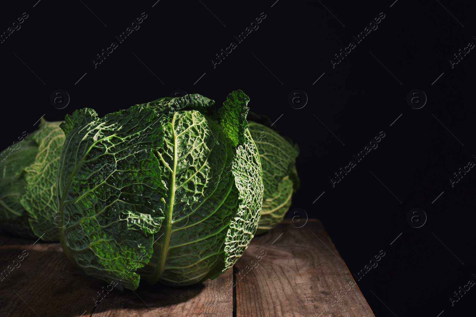 Photo of Savoy cabbage on wooden table against black background. Space for text