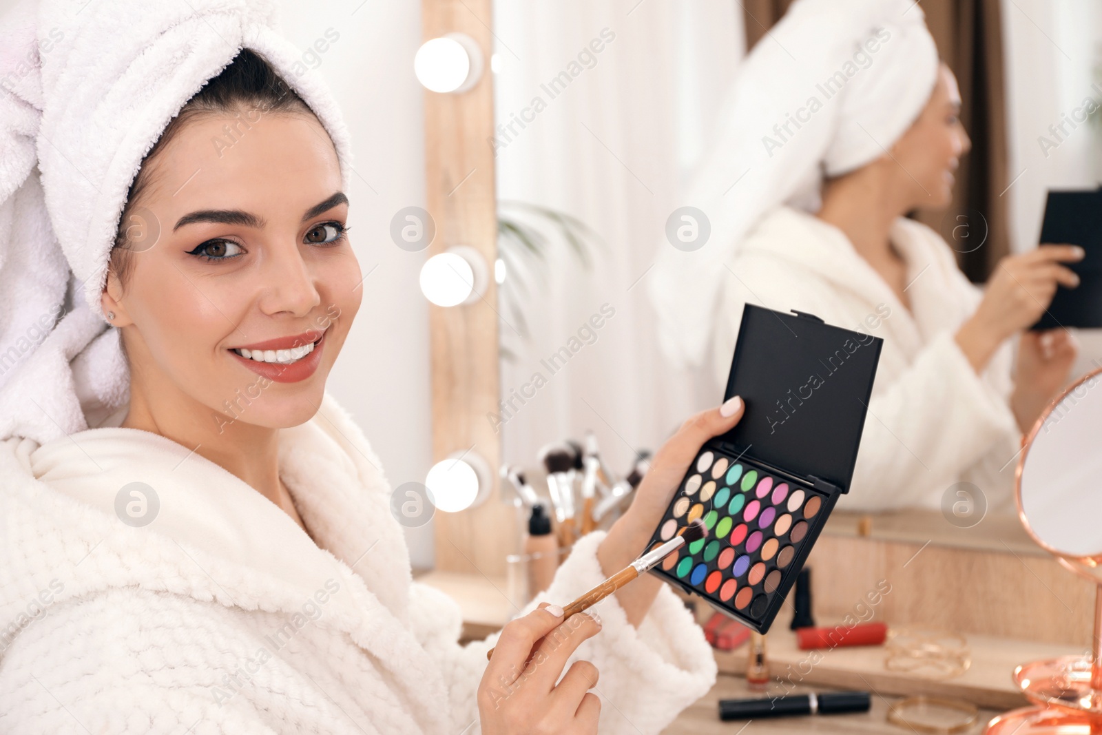 Photo of Beautiful woman applying makeup near mirror in room