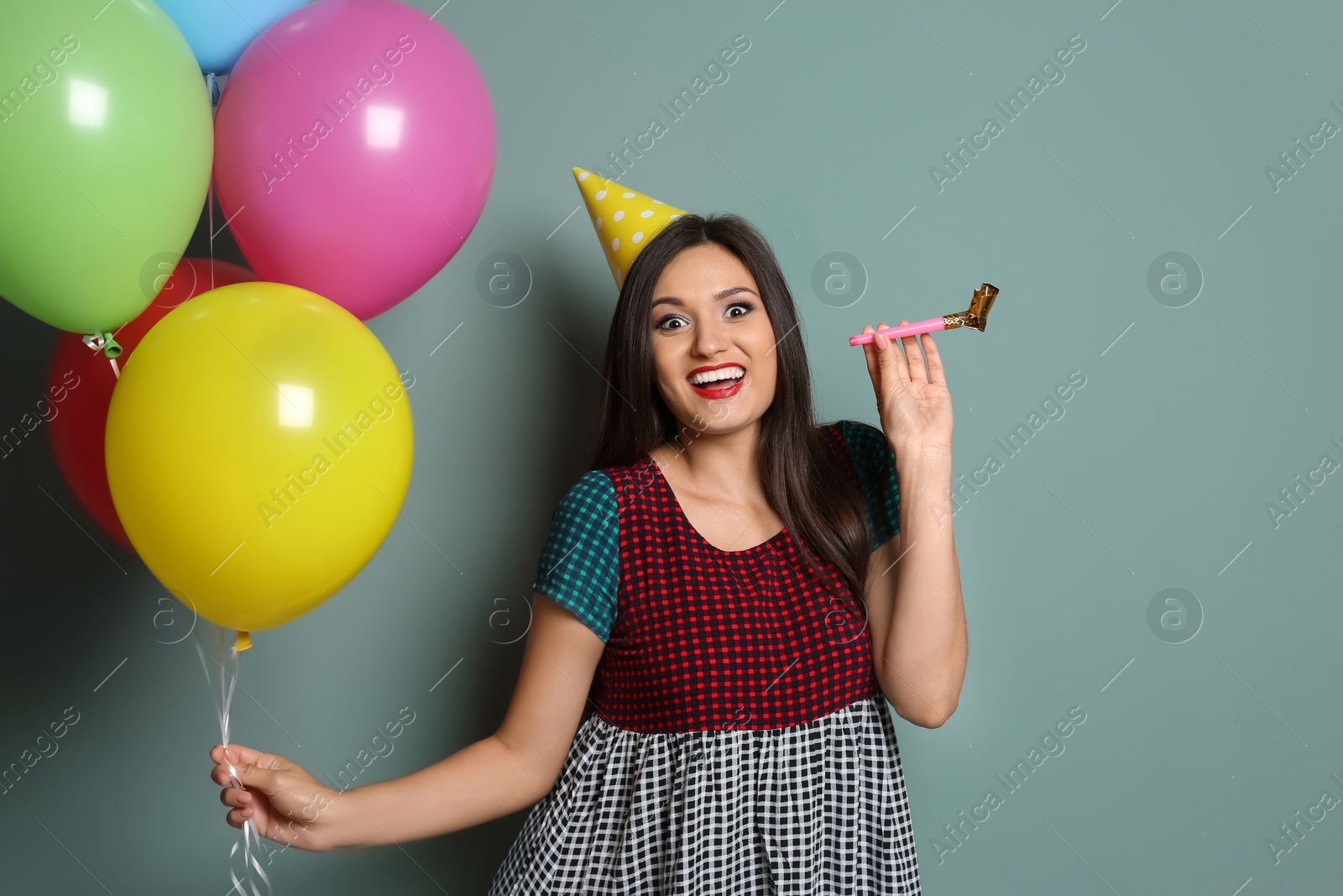 Photo of Young woman with bright balloons and party blower on color background. Birthday celebration