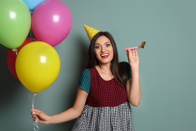 Young woman with bright balloons and party blower on color background. Birthday celebration